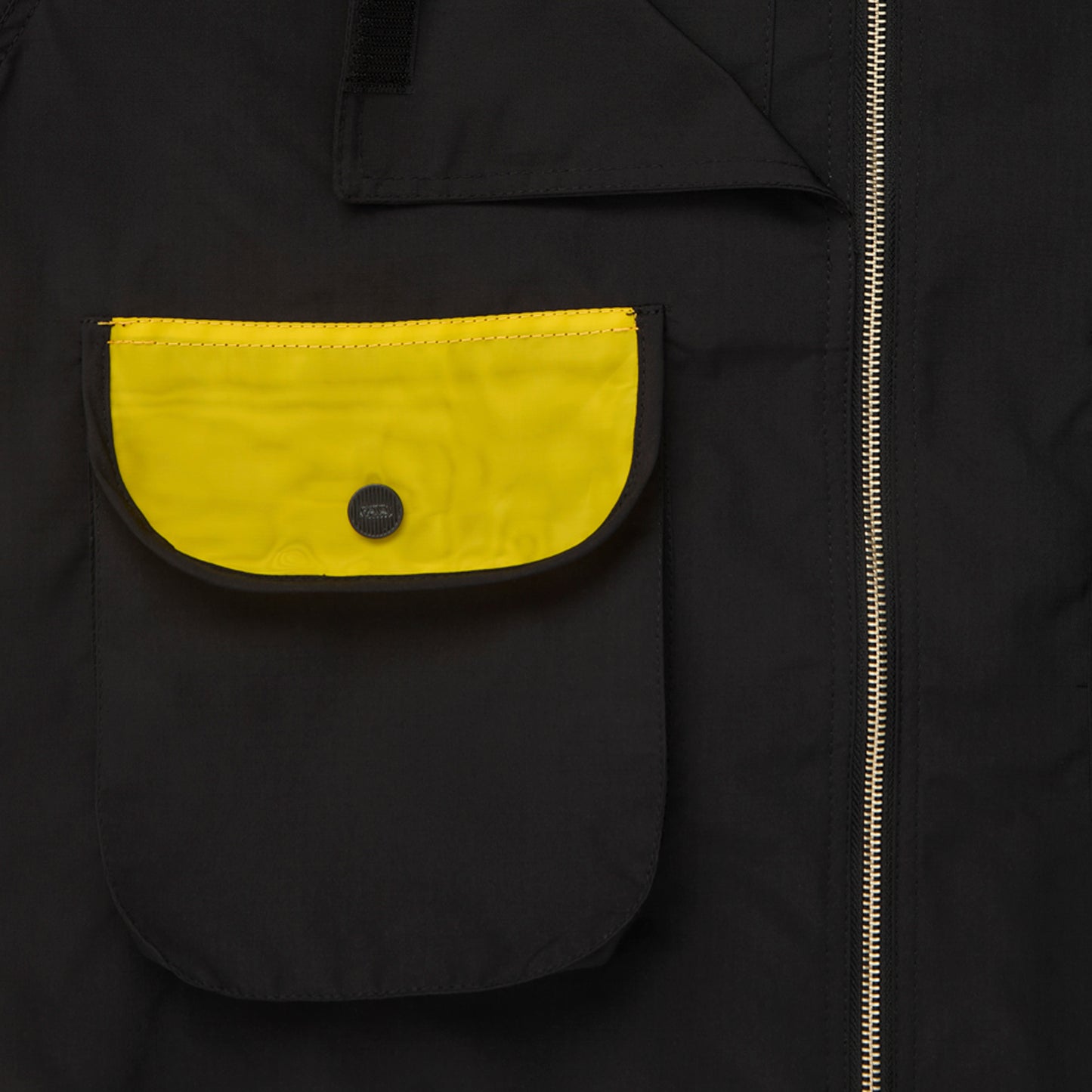 Bolso frontal da jaqueta preta com aba amarela e botão metálico