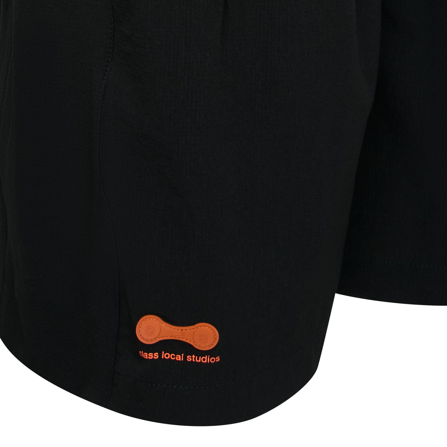 Barra de shorts preta com patch laranja e texto bordado discreto.