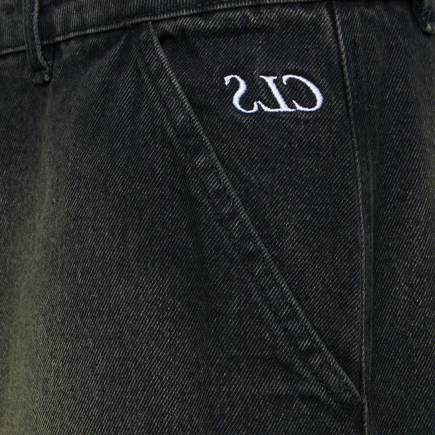 Close na costura e bordado de logo na calça jeans escura