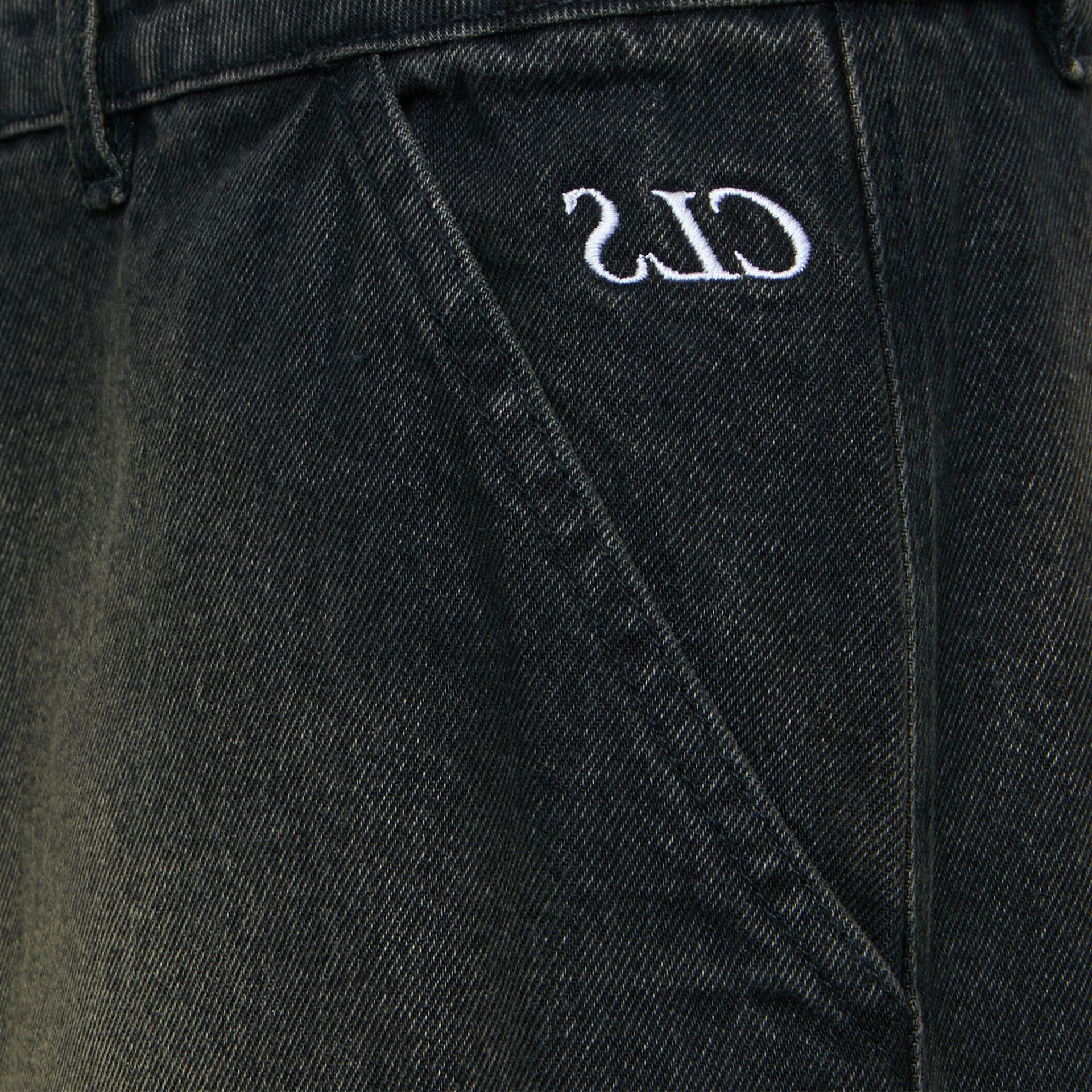Close na costura e bordado de logo na calça jeans escura