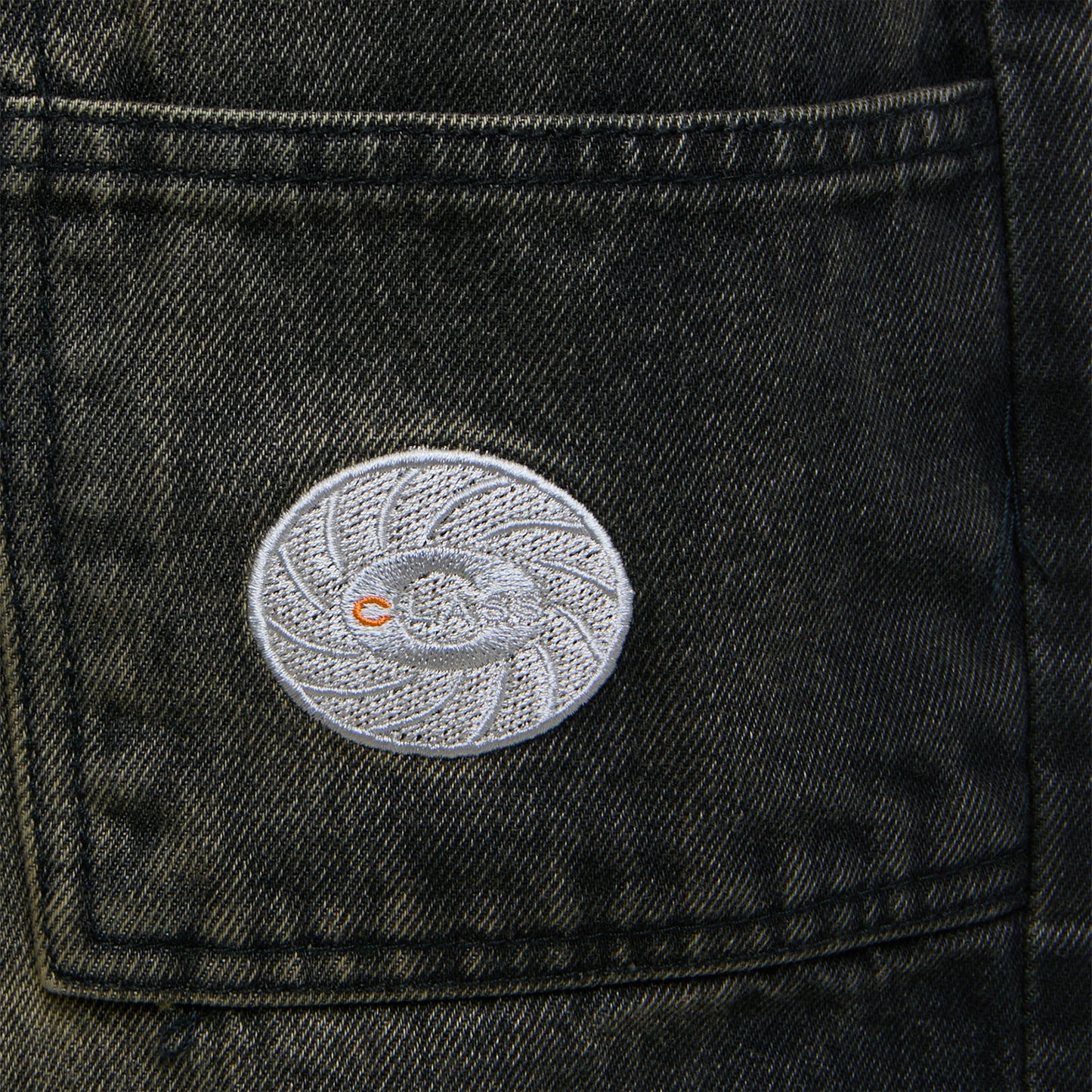 Patch oval bordado no bolso frontal da calça jeans escura