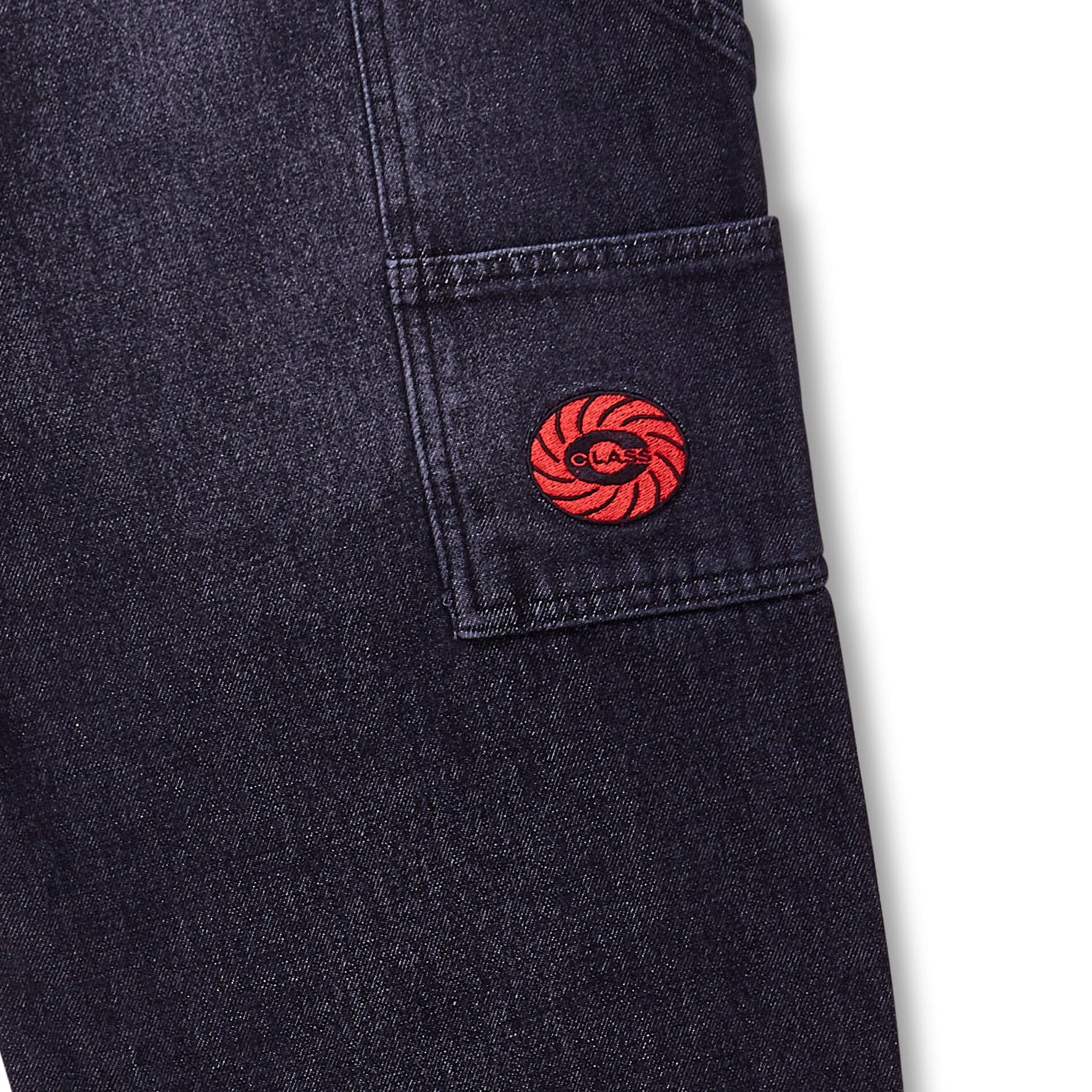 Calça jeans preta desbotada com bolso lateral e patch circular vermelho na barra.
