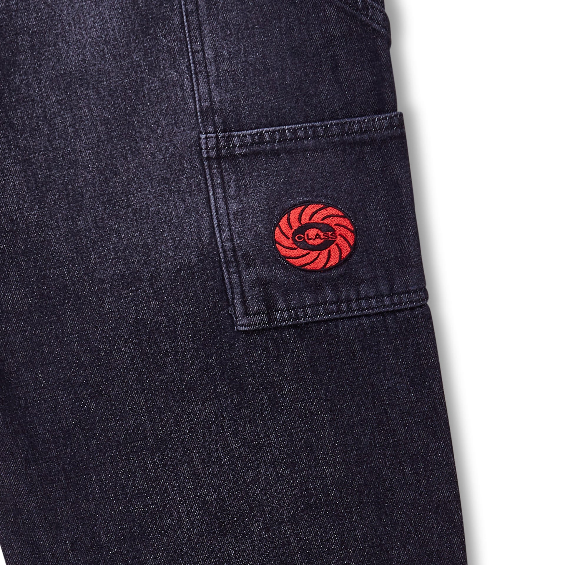 Calça jeans preta desbotada com bolso lateral e patch circular vermelho na barra.